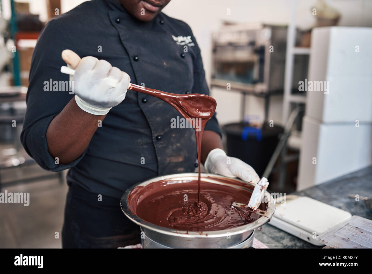 Travailleur ayant une cuillère pleine de chocolat fondu artisanale Banque D'Images