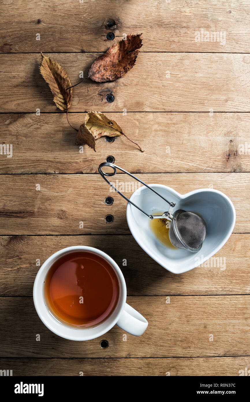 Une tasse de thé de fines herbes avec une crépine à mailles d'acier et les feuilles d'automne décoration de table. Banque D'Images
