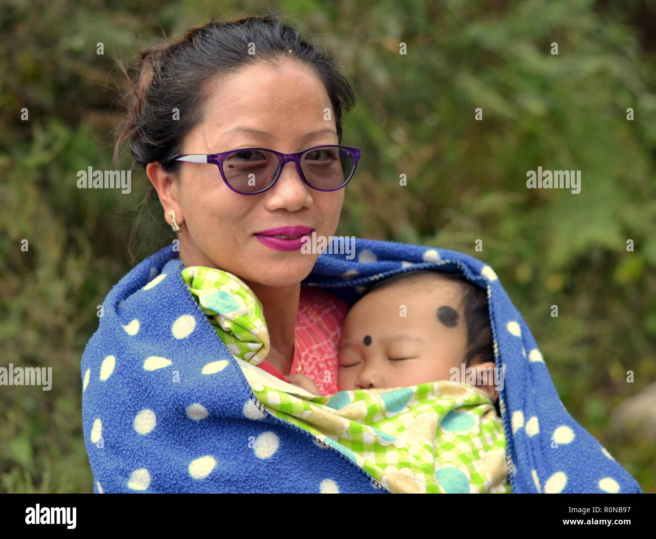 Les jeunes du nord-est de l'Inde des tribus Apatani femme de Ziro tient dans ses bras un bébé endormi avec deux points noirs de Kohl contre le mal des yeux (nazar) utarna. Banque D'Images