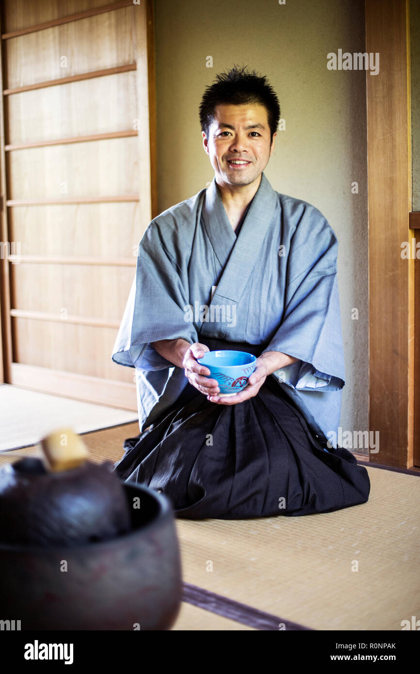 Homme portant un kimono traditionnel japonais à genoux sur le plancher,  holding blue Bol à thé pendant la cérémonie du thé Photo Stock - Alamy