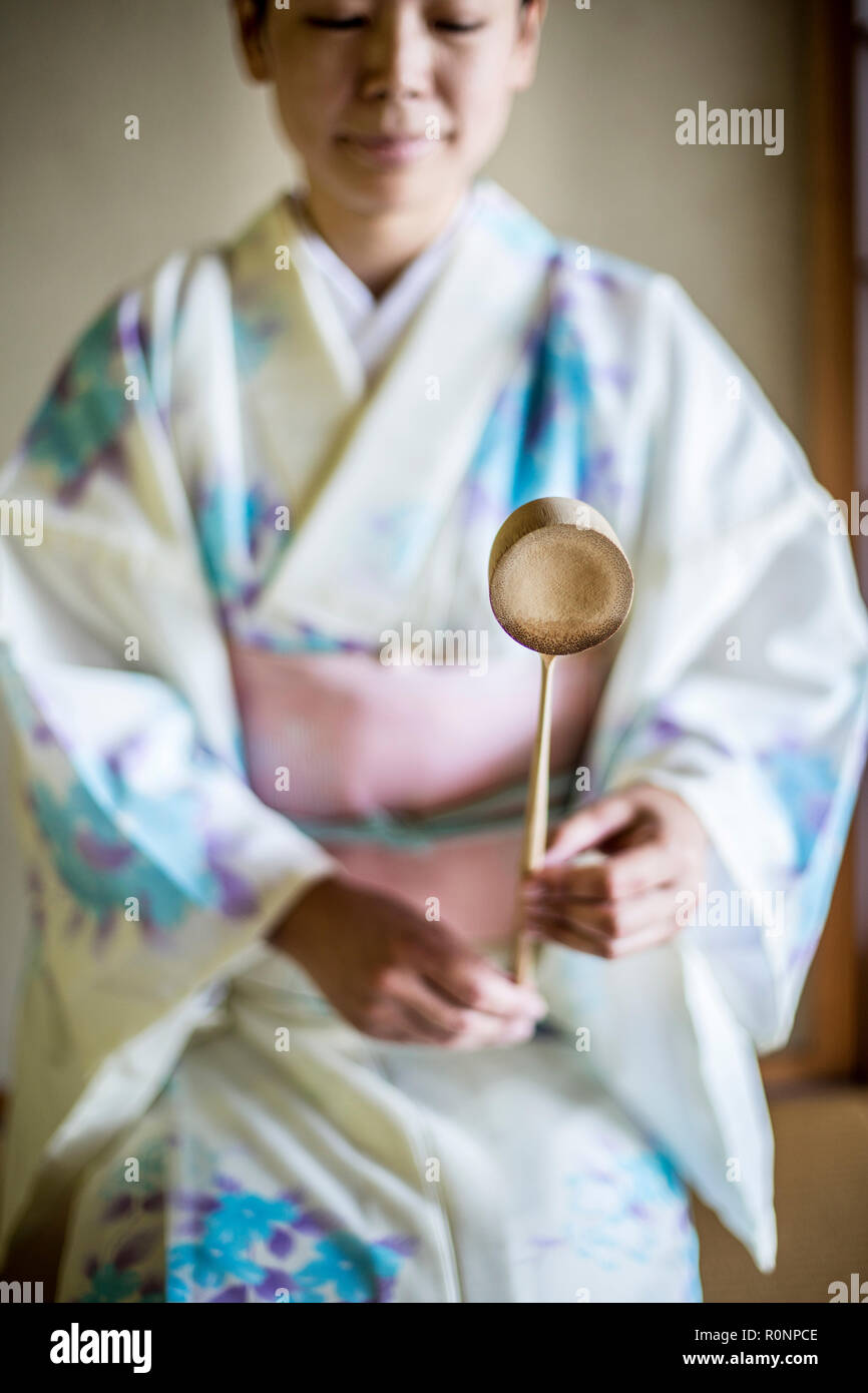 Japanese woman wearing kimono blanc traditionnel avec motif floral bleu à genoux sur marbre au cours de cérémonie du thé, tenant une Hishaku, une louche de bambou. Banque D'Images