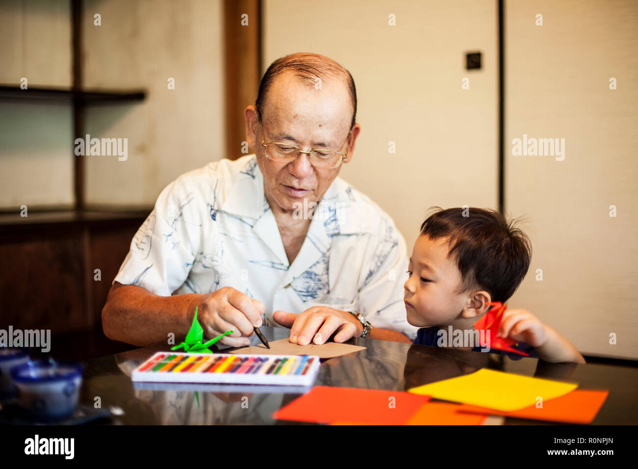 L'homme japonais et petit garçon assis à une table, faisant de l'Origami animaux en utilisant du papier de couleur vive. Banque D'Images