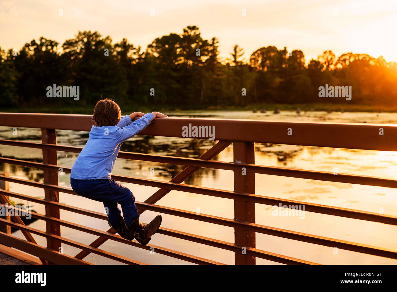 Garçon escalade sur une rambarde du pont au coucher du soleil, United States Banque D'Images