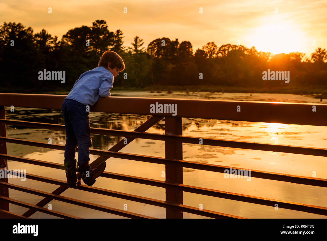 Garçon escalade sur une rambarde du pont au coucher du soleil, United States Banque D'Images