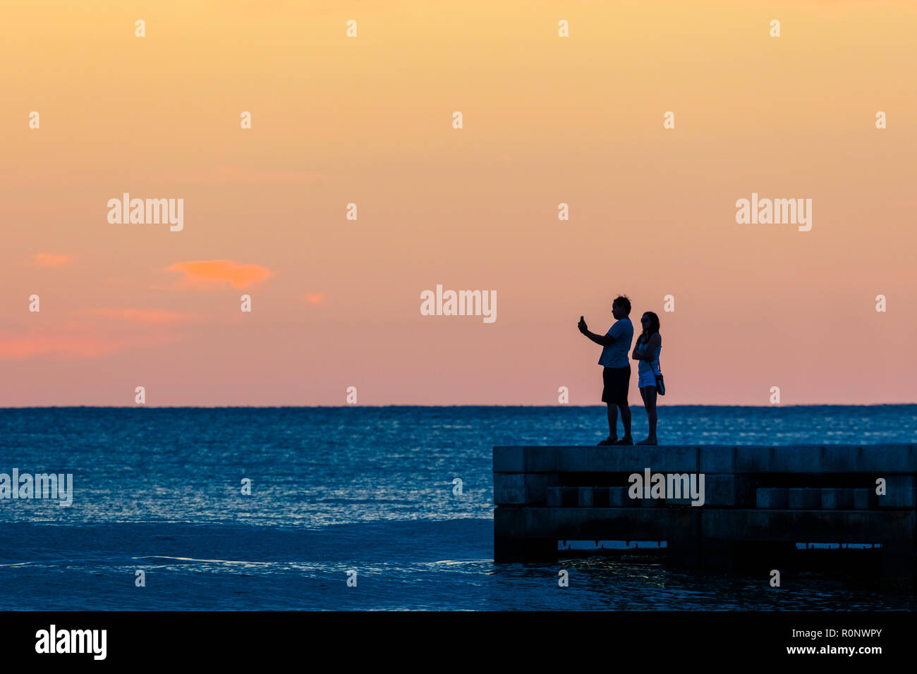 Couple qui se profilant selfies contre un ciel coucher de soleil orange sur le golfe du Mexique dans le sud-ouest de la Floride, États-Unis Banque D'Images