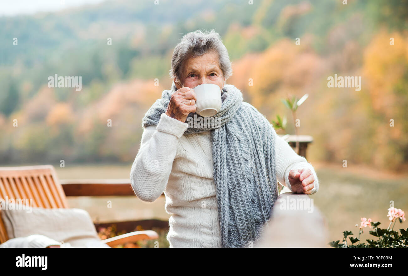 Une vieille femme de boire du café en plein air sur une terrasse en automne. Banque D'Images