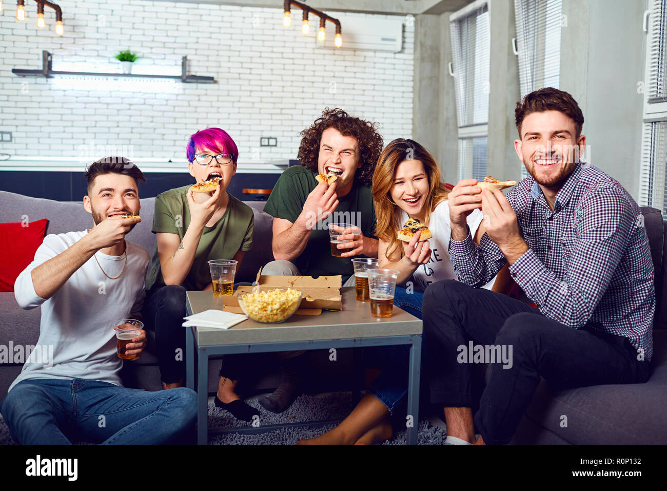 Un groupe d'amis eating pizza wathing plat assis sur le canapé. Banque D'Images