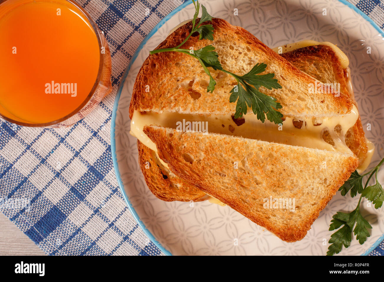 Tranches de pain grillé avec du fromage et persil vert sur plaque blanche, verre de jus d'orange avec une serviette de cuisine bleu. De la bonne nourriture pour le petit déjeuner. Haut de la vie Banque D'Images