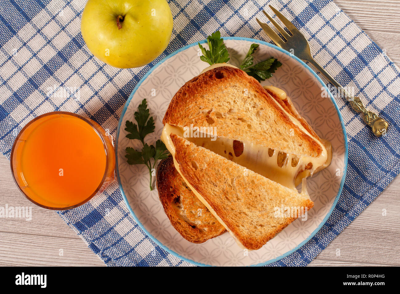 Tranches de pain grillé avec du fromage et persil vert sur plaque blanche, fourchette, verre de jus d'orange et de pomme verte avec une serviette de cuisine bleu. La bonne nourriture Banque D'Images