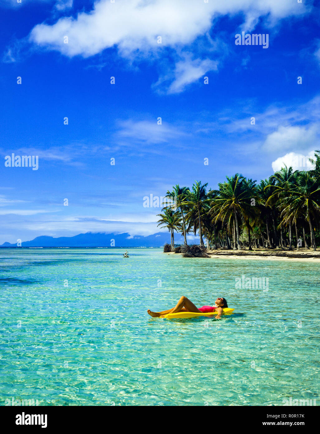 Jeune femme en maillot rouge sur jaune soleil matelas d'air, flottant sur la mer des Caraïbes, la plage tropicale, palmiers, Guadeloupe, French West Indies, Banque D'Images