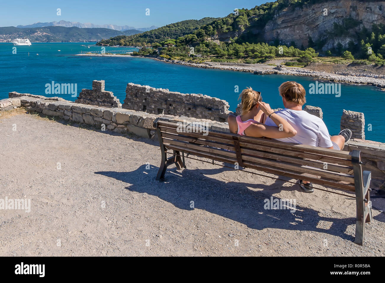 Jeune couple assis sur un banc, admire la vue sur le Golfe des Poètes à Portovenere avec un bateau de croisière dans l'arrière-plan, ligurie, italie Banque D'Images