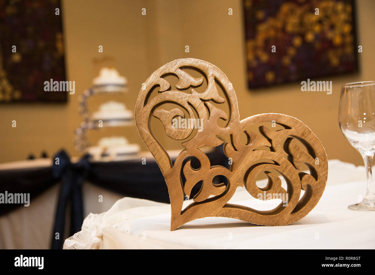 Coeur en bois sculpté à l'avant-plan avec trois niveaux gâteau de mariage blanc en arrière-plan Banque D'Images