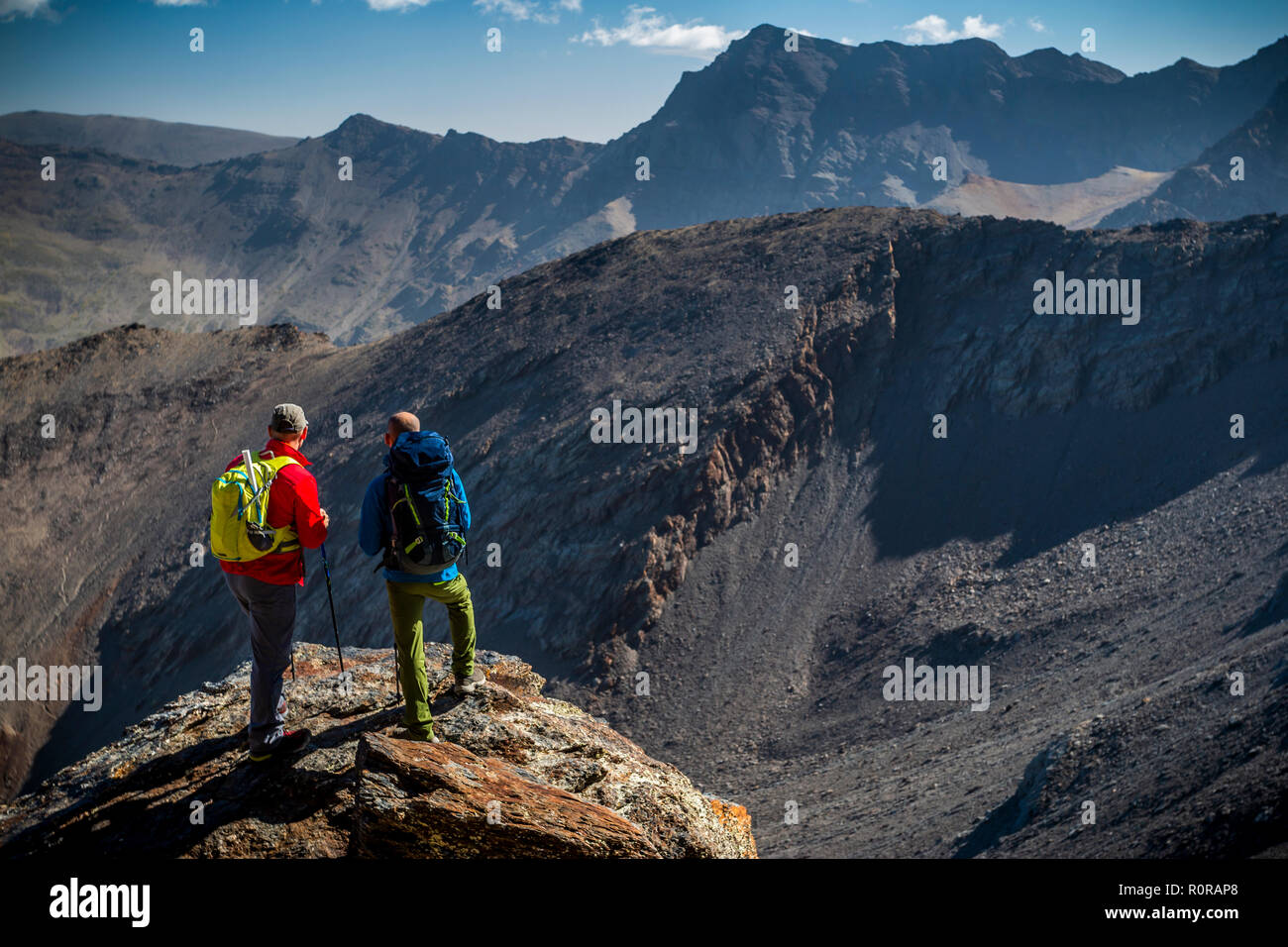 Vue arrière de deux voyageurs masculins debout sur rock et en regardant les montagnes magnifiques sur belle journée ensoleillée en Sierra Nevada, Granada, Espagne Banque D'Images
