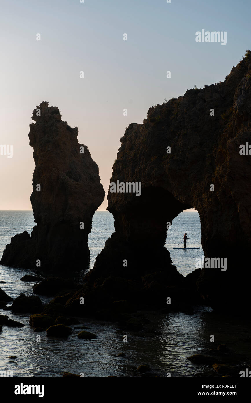 L'homme sur un SUP StandUpPaddle derrière un rocher arch, rochers dans la mer, Algarve côte rock, Ponta da Piedade, Lagos, Portugal Banque D'Images