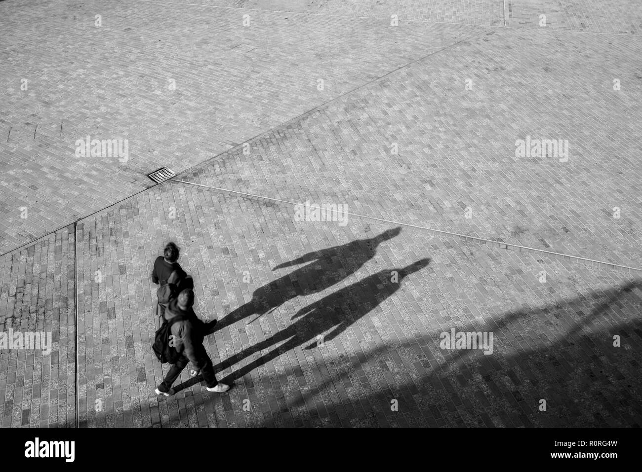 Couple de floue méconnaissable au-dessus de la marche sur un espace ouvert carré avec la projection des ombres sur le sol Banque D'Images