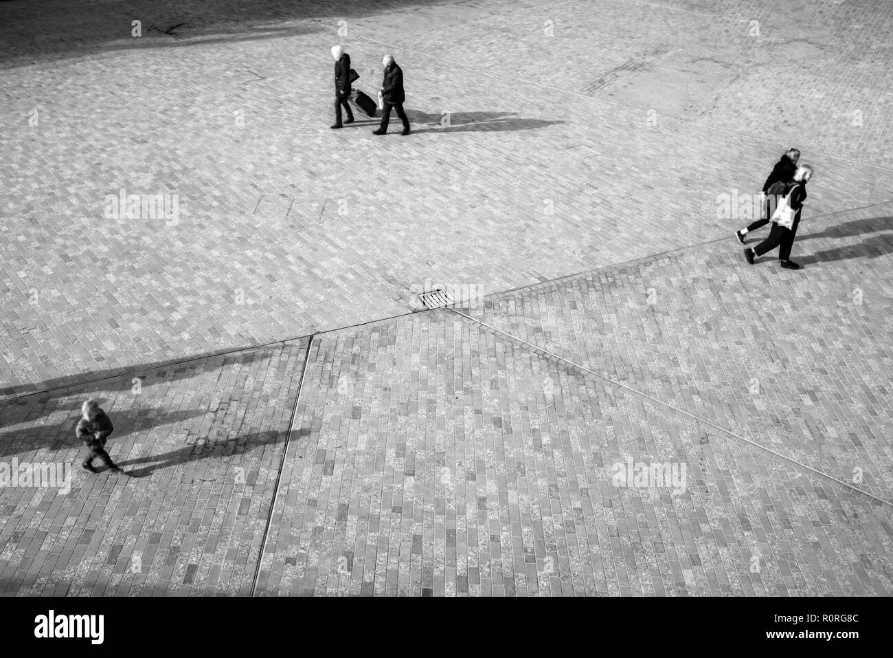 Les gens d'en haut trouble méconnaissable marche sur un espace ouvert carré avec la projection des ombres sur le sol Banque D'Images