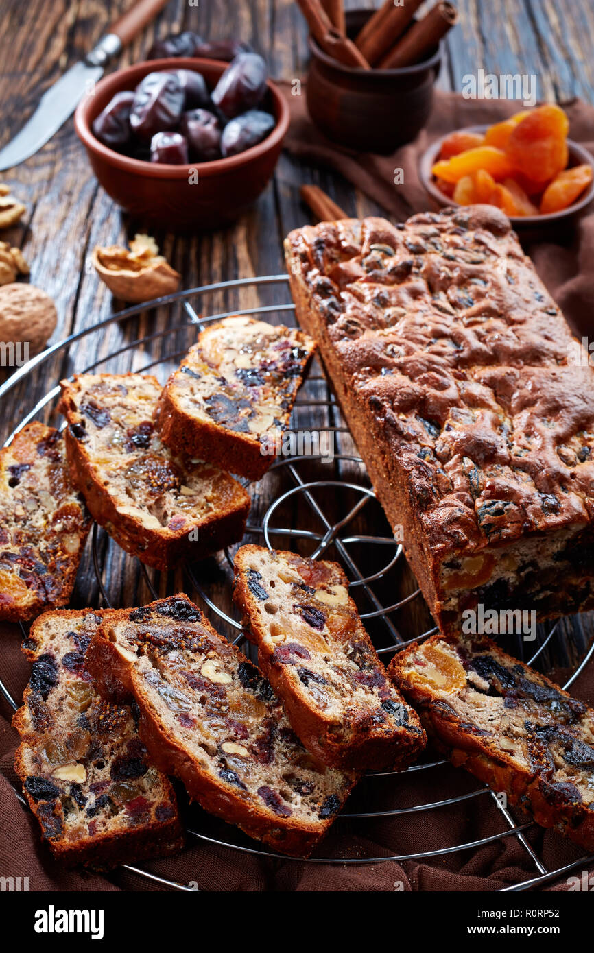 Fruits secs gâteau riche sur un fil cake stand avec tissu marron, des bâtons de cannelle, des abricots séchés et date fruits sur une table en bois rustique, vue verticale Banque D'Images