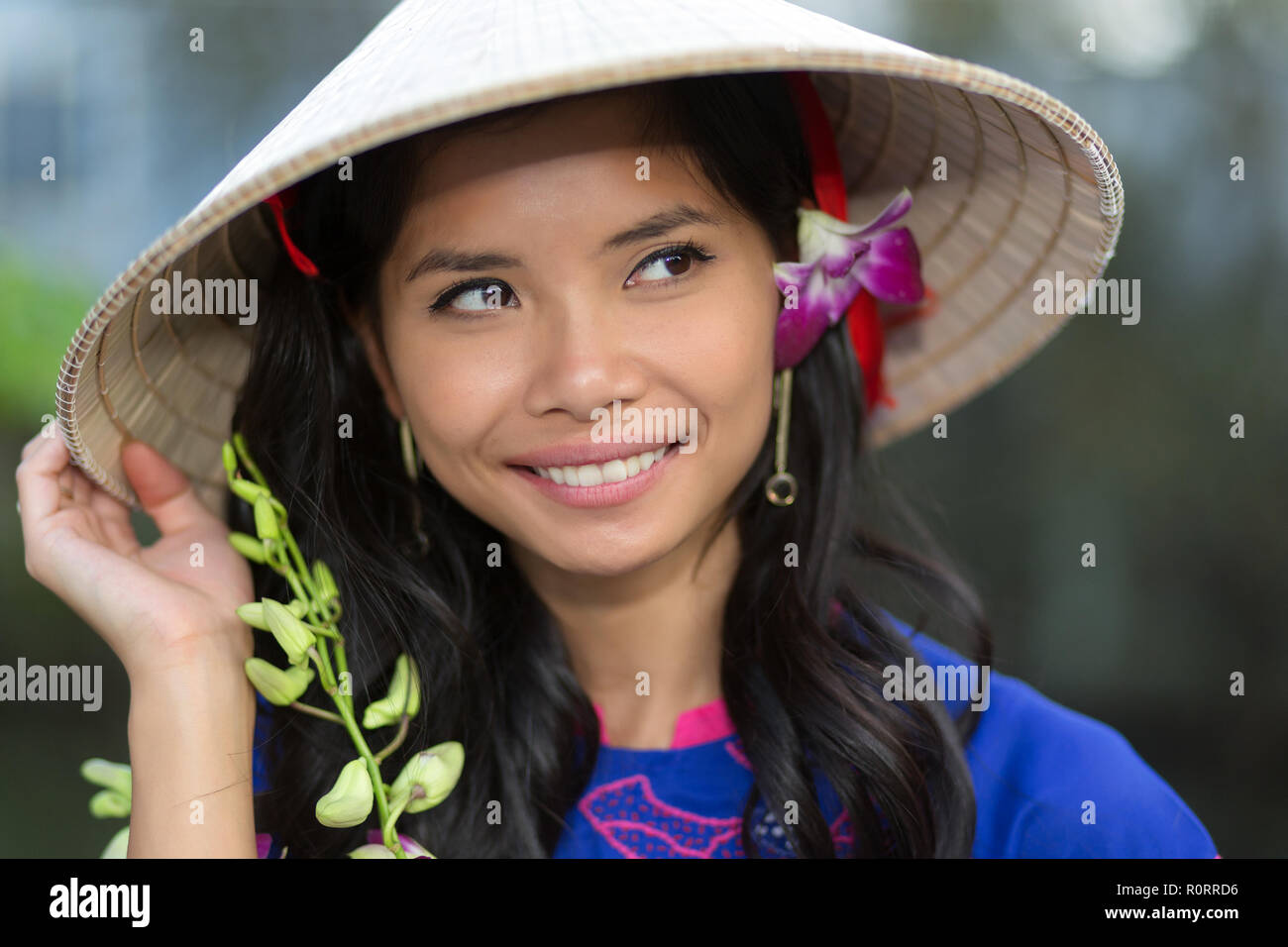 Jolie femme vietnamienne portant un chapeau conique traditionnel avec une  fleur dans ses cheveux en souriant heureusement qu'elle en a l'air dans  l'air Photo Stock - Alamy