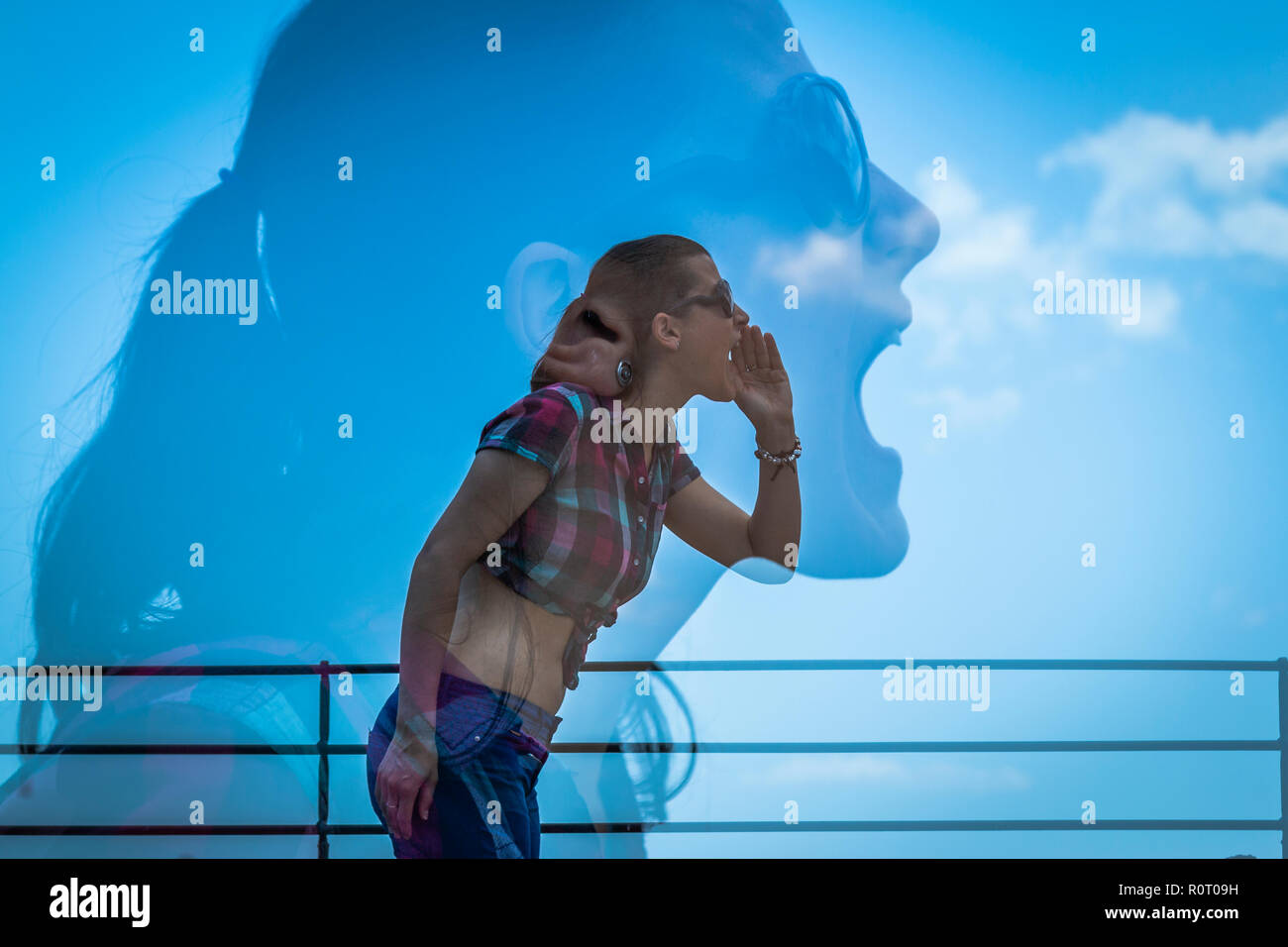 Vue latérale des jeunes femmes en tenue décontractée en gardant la main près de la bouche et crier alors que sur fond de projection d'elle-même et ciel bleu Banque D'Images