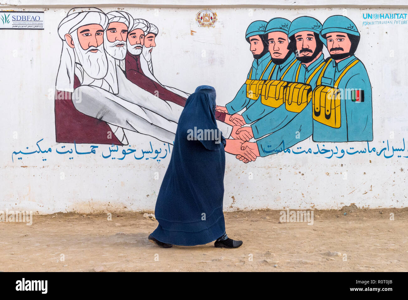 Femme marche parrainée par la propagande naïve peinture murale sur le côté de la rue sur l'armée et les clercs qui s'occupent du Peuple, Mazar-e Sharif, Afghanistan Banque D'Images