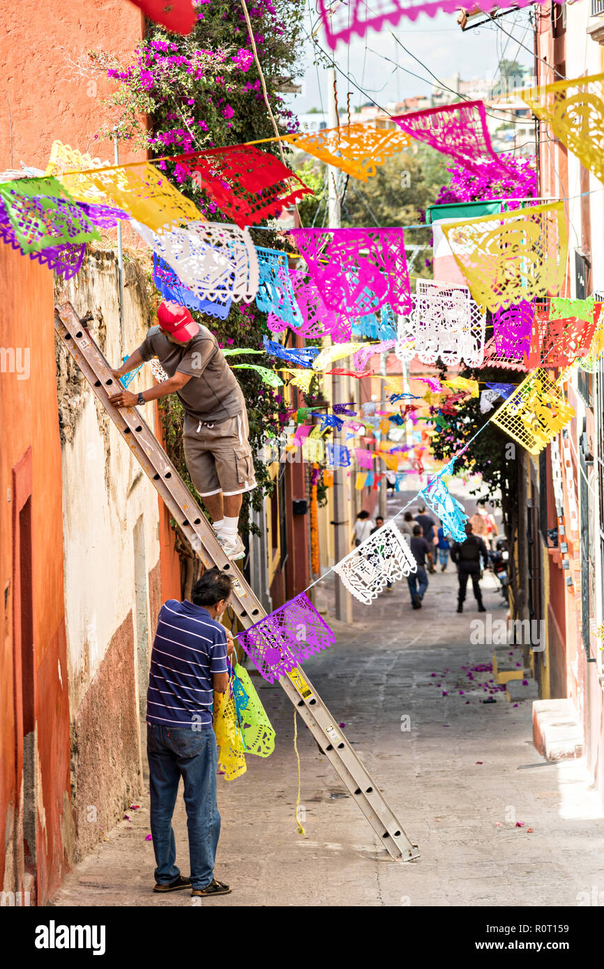 Chaîne de papel picado travailleurs à travers des bannières d'une allée en préparation d'une procession des Morts Morts au cours de la Dia de muertos festival à San Miguel de Allende, Mexique. Le festival de plusieurs jours est de se souvenir de leurs amis et les membres de leur famille qui sont morts à l'aide de comté, aztec tagètes, alfeniques, papel picado et les aliments et boissons préférés des défunts. Banque D'Images