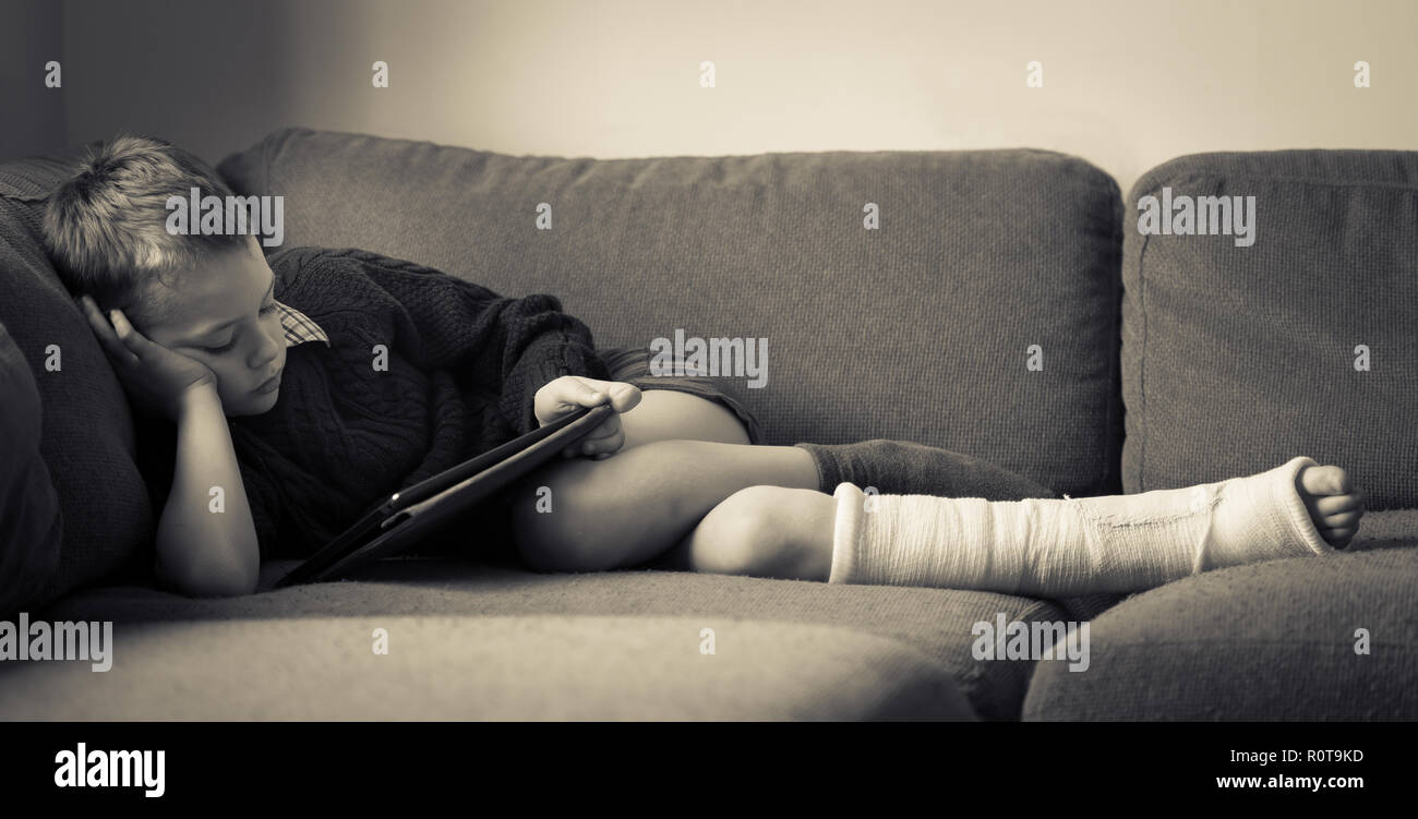 un-petit-garcon-avec-le-tdah-l-autisme-le-syndrome-d-asperger-la-lecture-d-un-livre-sur-le-canape-apres-s-etre-casse-la-jambe-et-l-avoir-mis-dans-le-platre-a-l-hopital-r0t9kd.jpg