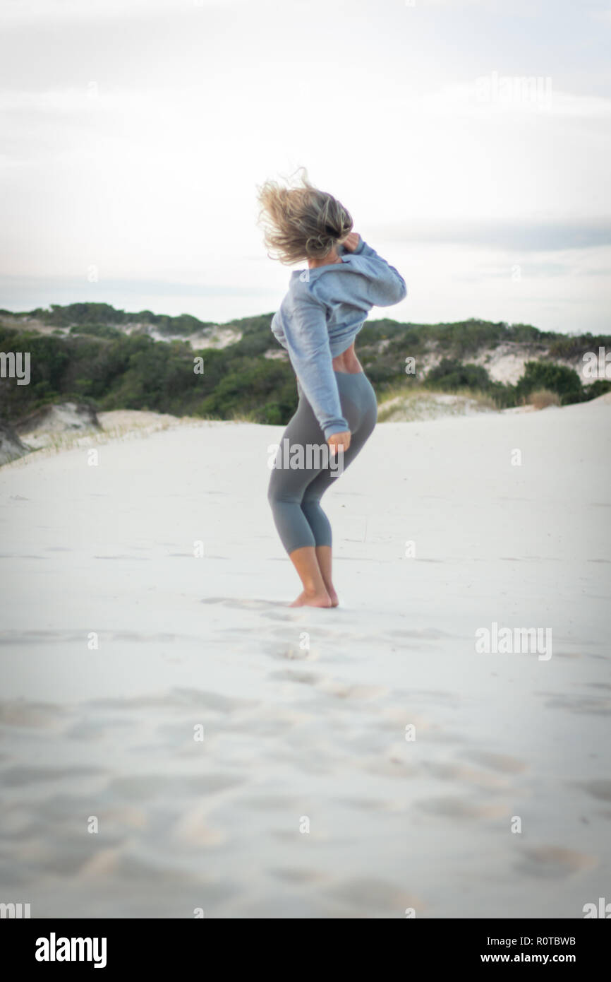 Femme blonde avec les tenues de sauter et danser sur une dune de sable blanc Banque D'Images