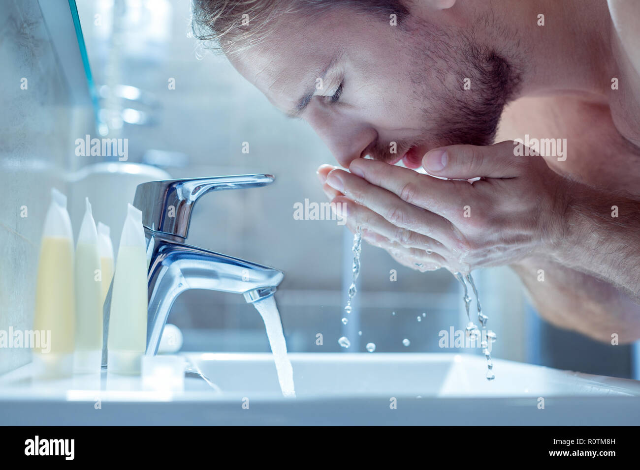 Bel homme barbu lave son visage le matin dans la salle de bains lumière Banque D'Images