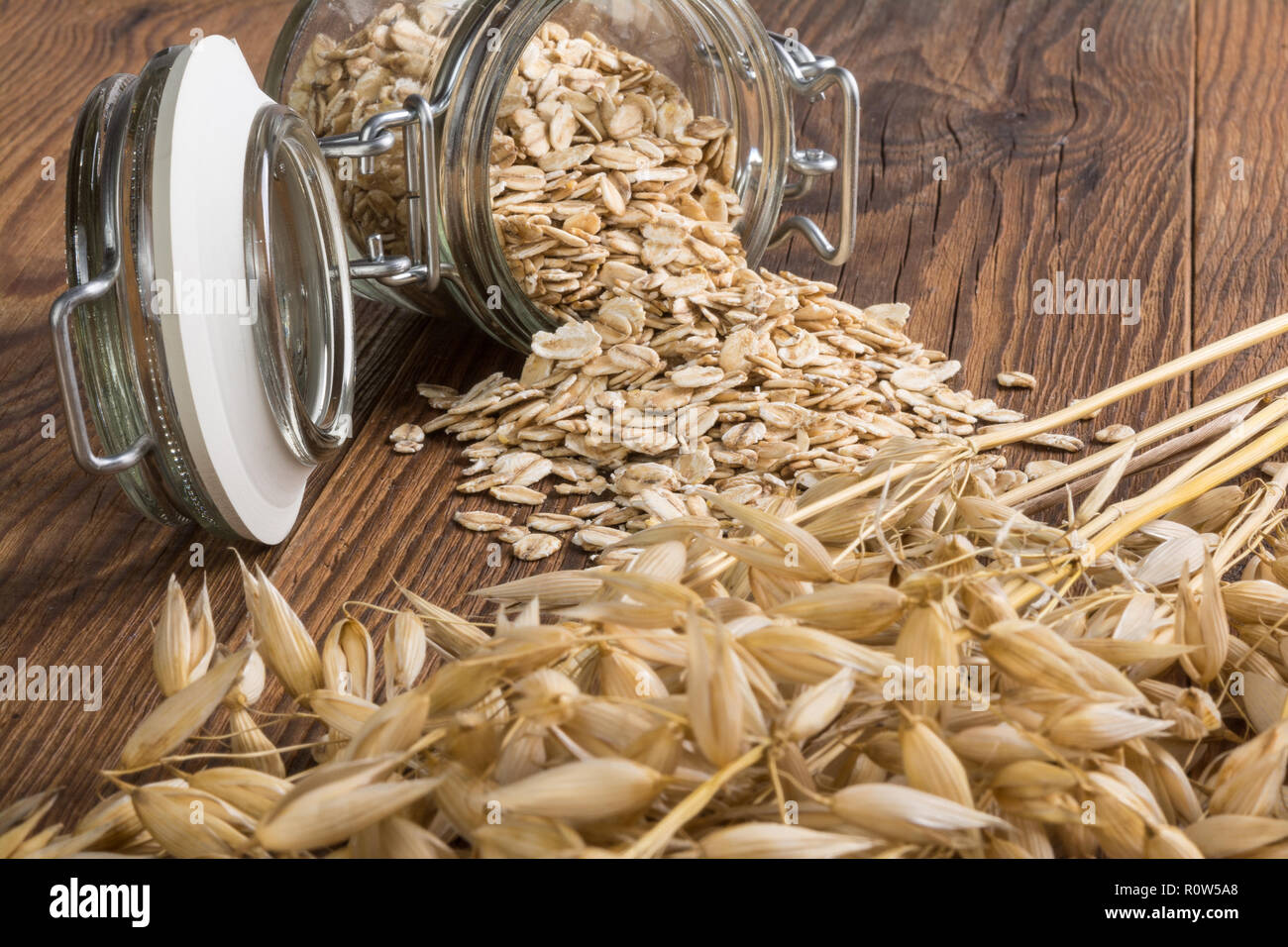 Les flocons d'avoine et les oreilles à sec sur la table en bois. L'avoine commune. Avena sativa. Belle close-up d'un bocal de verre allongé. Flocons de céréales sèches, renversé des pointes, des céréales. Banque D'Images