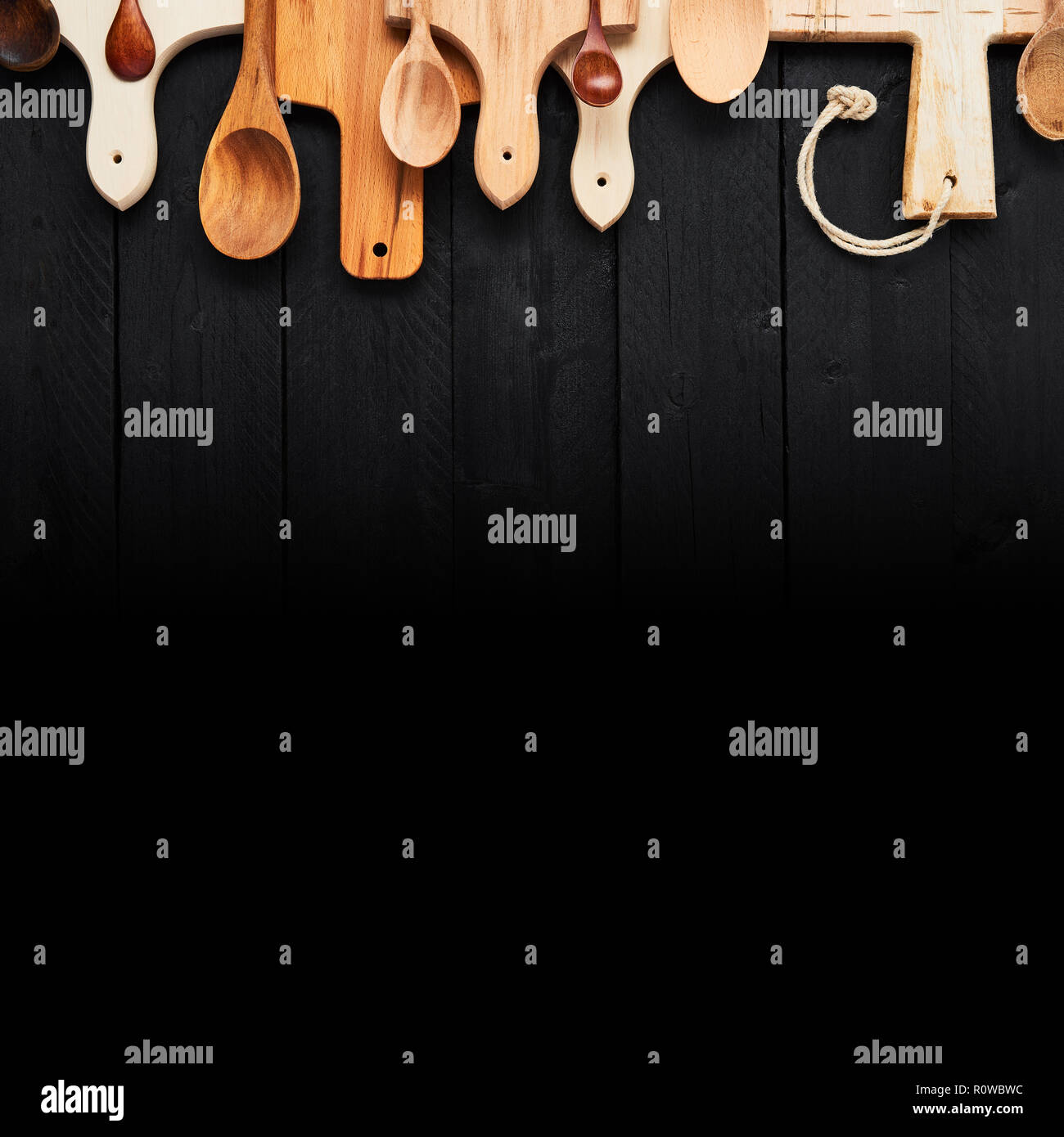 Vue du dessus de l'assortiment de cuillères en bois et planches à découper sur la table en bois noir avec black gradient. Concept d'arrière-plan de l'alimentation. Copier l'espace. Banque D'Images