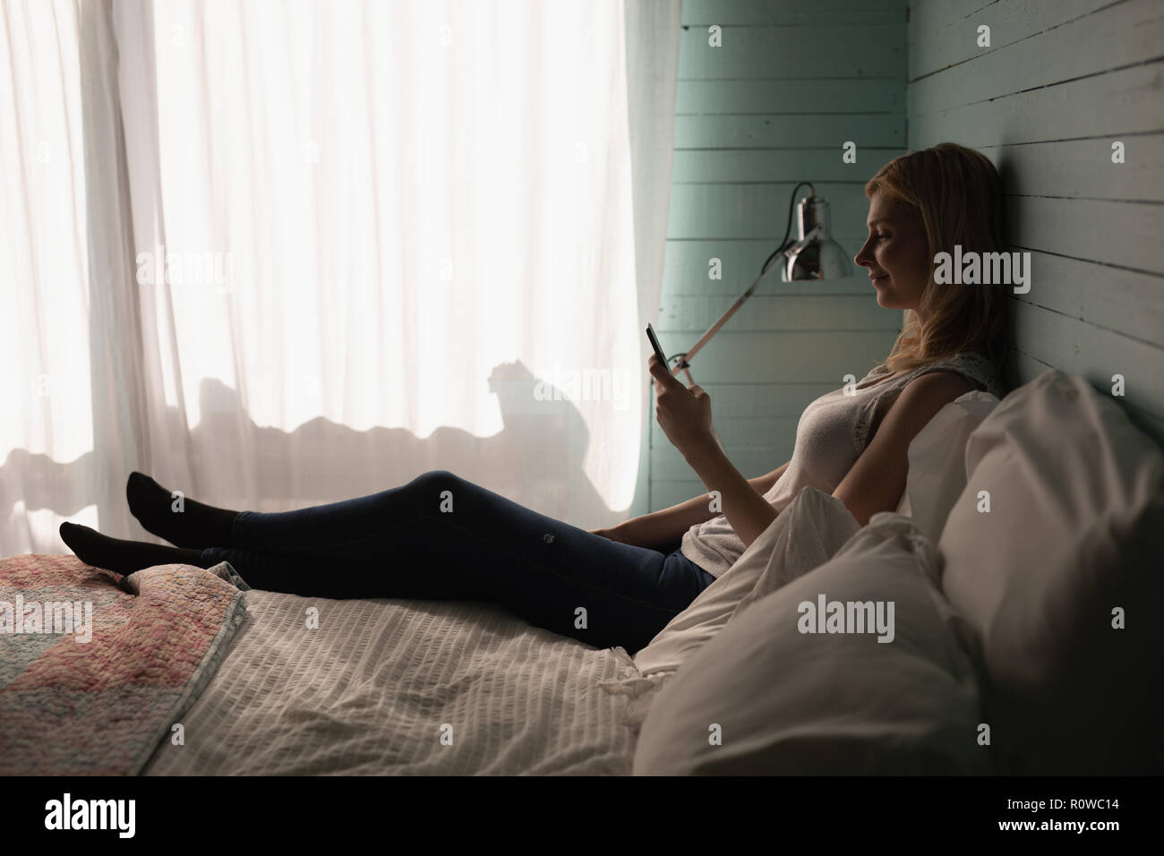 Woman using mobile phone in bedroom Banque D'Images