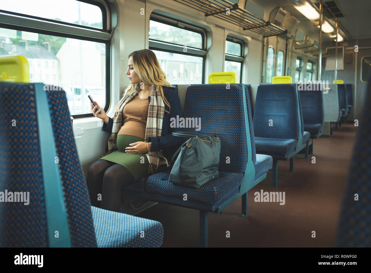 Femme enceinte à l'aide de téléphone portable en voyage en train Banque D'Images