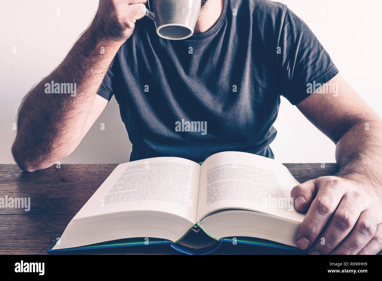 Man reading book at table de cuisine tout en buvant du café Banque D'Images