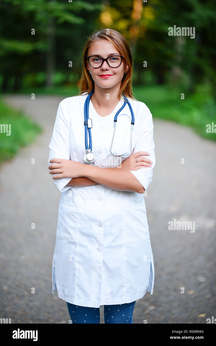 Une jeune fille qui est médecin se trouve à l'extérieur, bras croisés sur le ventre. Banque D'Images
