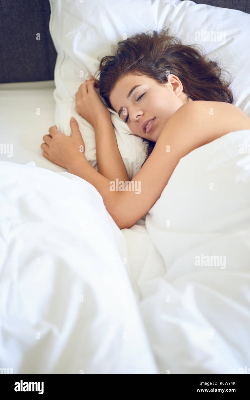 Belle jeune femme latine femme aux longs cheveux brun couché dans son lit de draps blancs smiling at the camera Banque D'Images