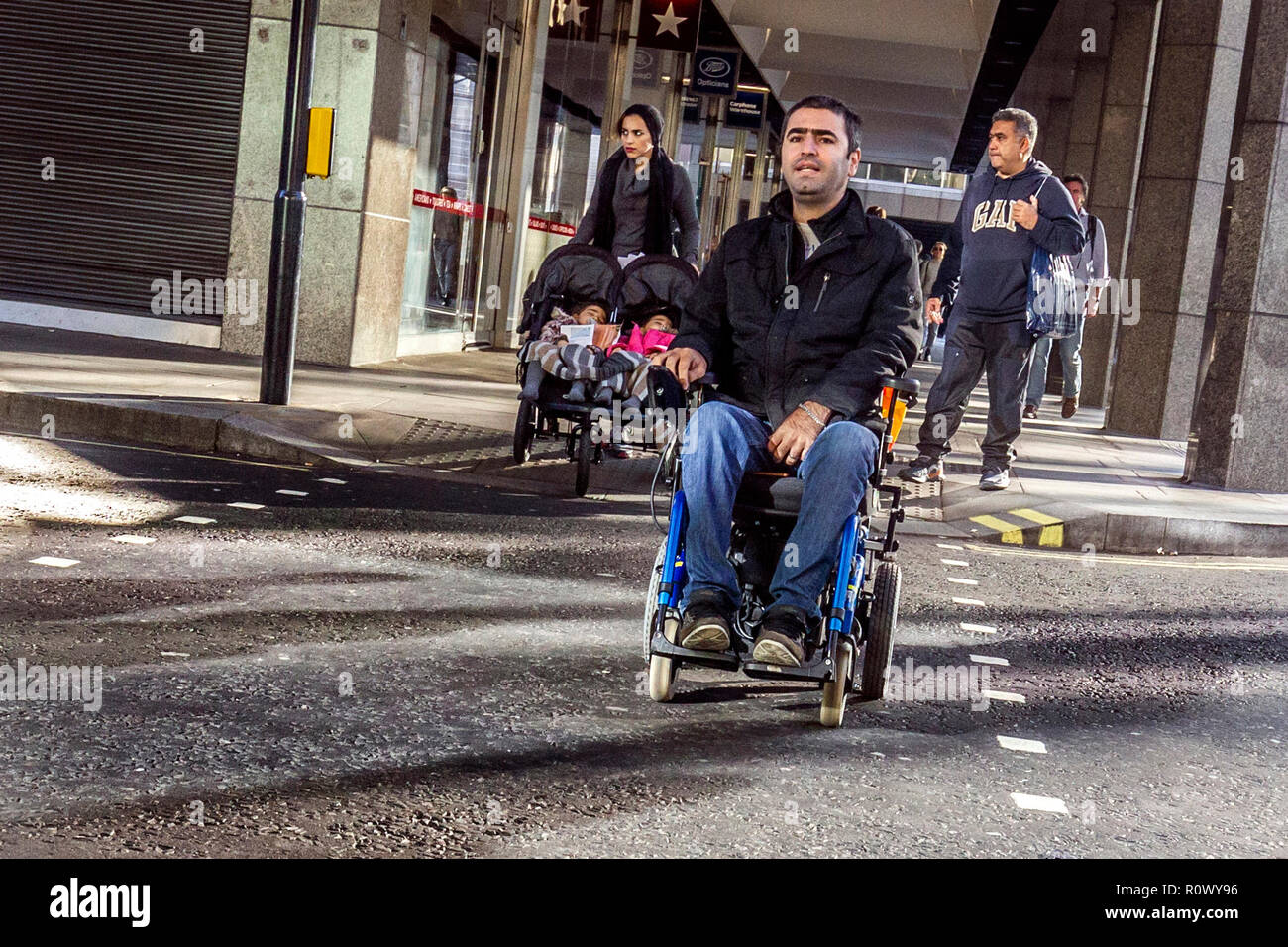 Homme handicapé en fauteuil roulant motorisé crossing Road à Londres, Royaume-Uni. Banque D'Images