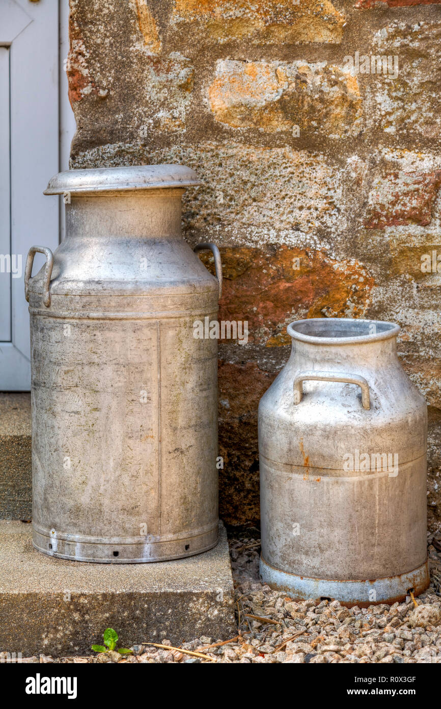 Deux bidons de lait traditionnel sur une porte, agsinst d'un mur de pierre. Banque D'Images