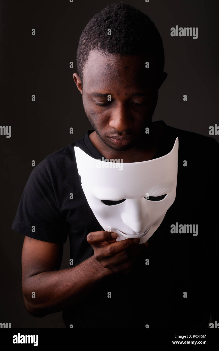 Studio shot of young black African man in dark room holding mask Banque D'Images