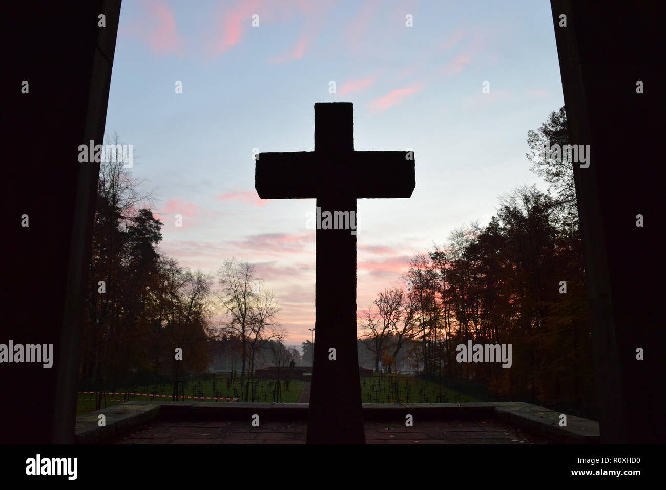 L'échéancier de l'matin ciel crépuscule vu de derrière une croix en pierre de sable au cours de sculpture le soleil levant dans le cimetière militaire Reimsbach an der Saar. Banque D'Images