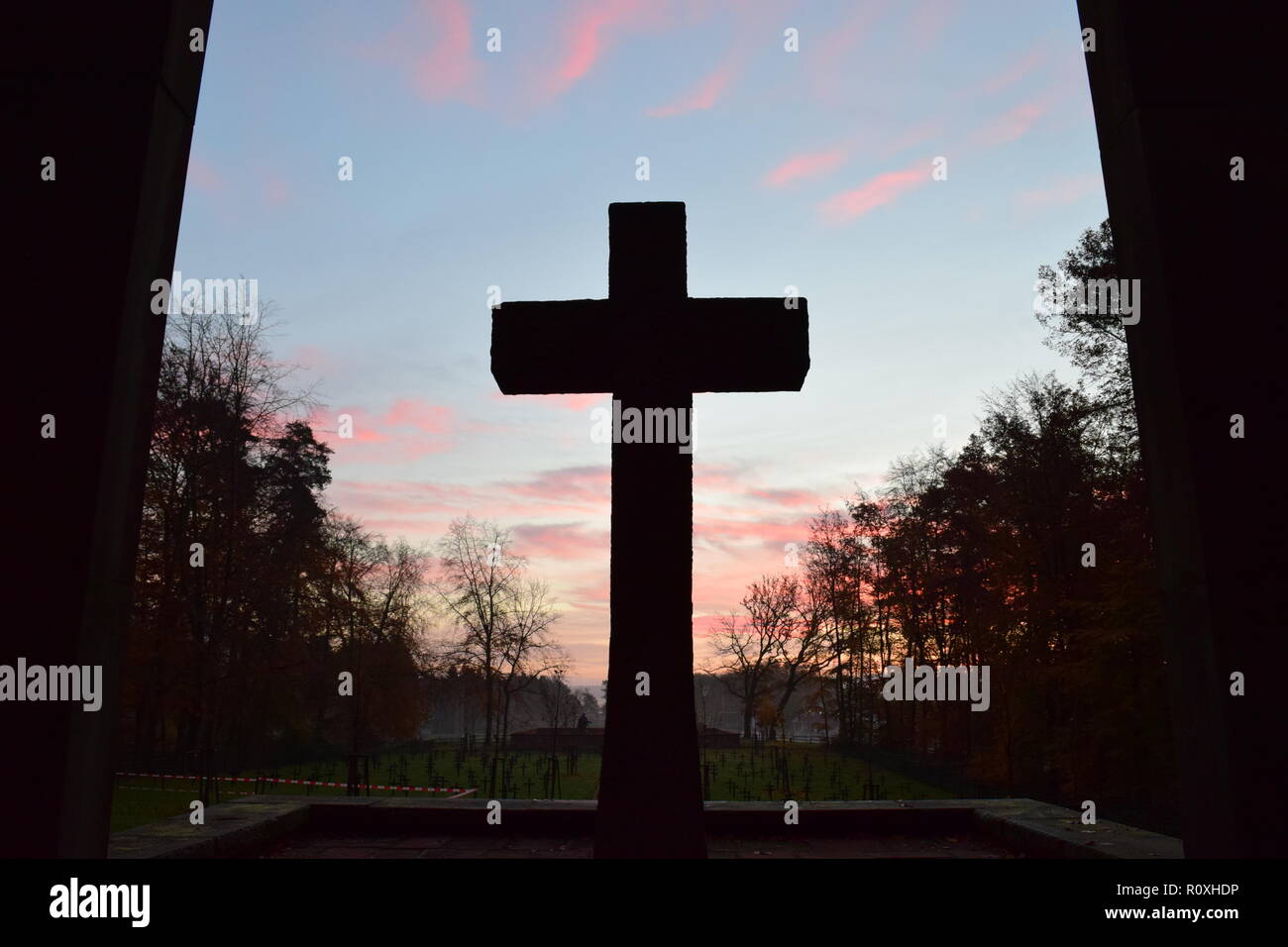 L'échéancier de l'matin ciel crépuscule vu de derrière une croix en pierre de sable au cours de sculpture le soleil levant dans le cimetière militaire Reimsbach an der Saar. Banque D'Images