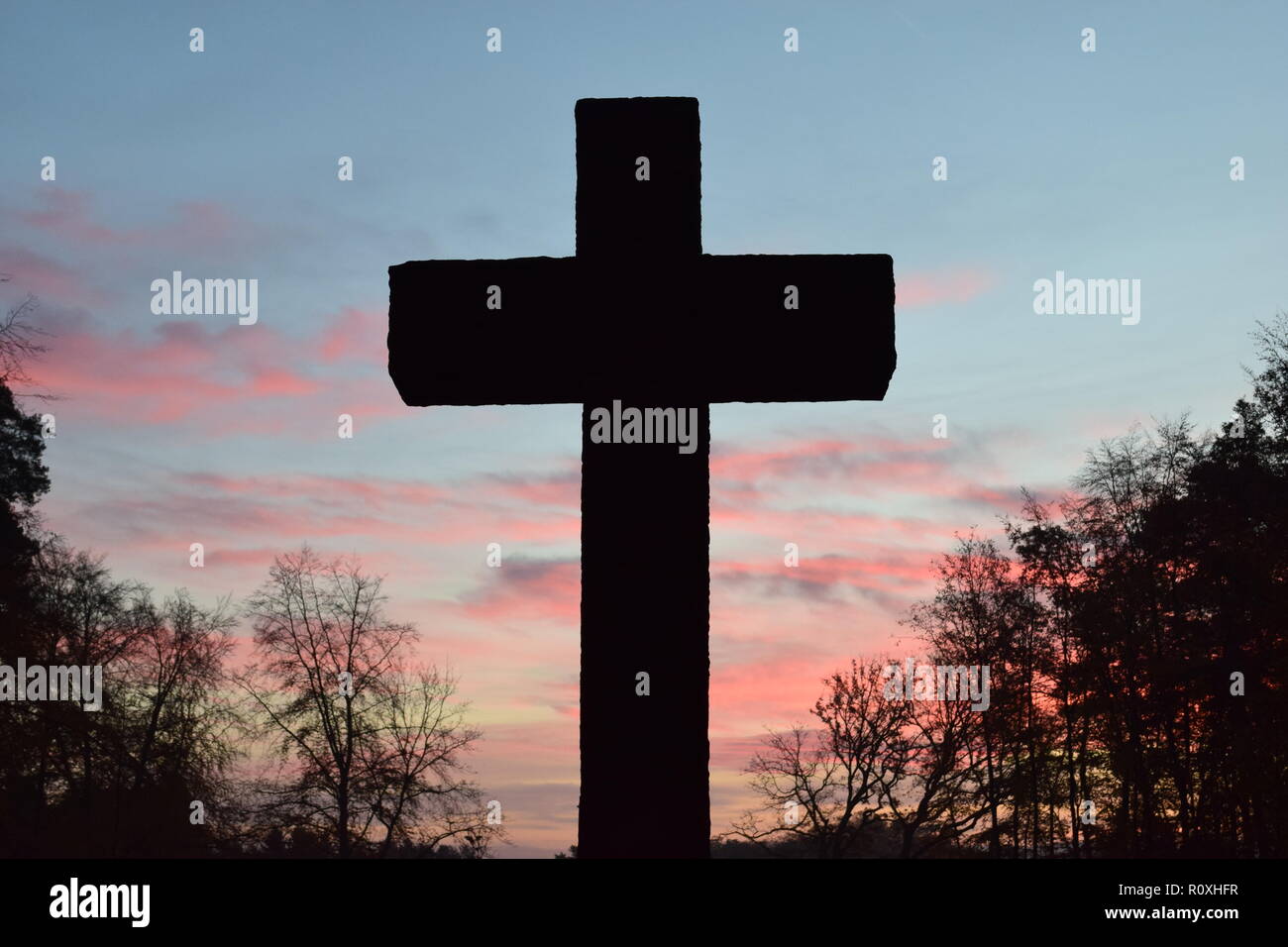 L'échéancier de l'matin ciel crépuscule vu de derrière une croix en pierre de sable au cours de sculpture le soleil levant dans le cimetière militaire Reimsbach an der Saar. Banque D'Images