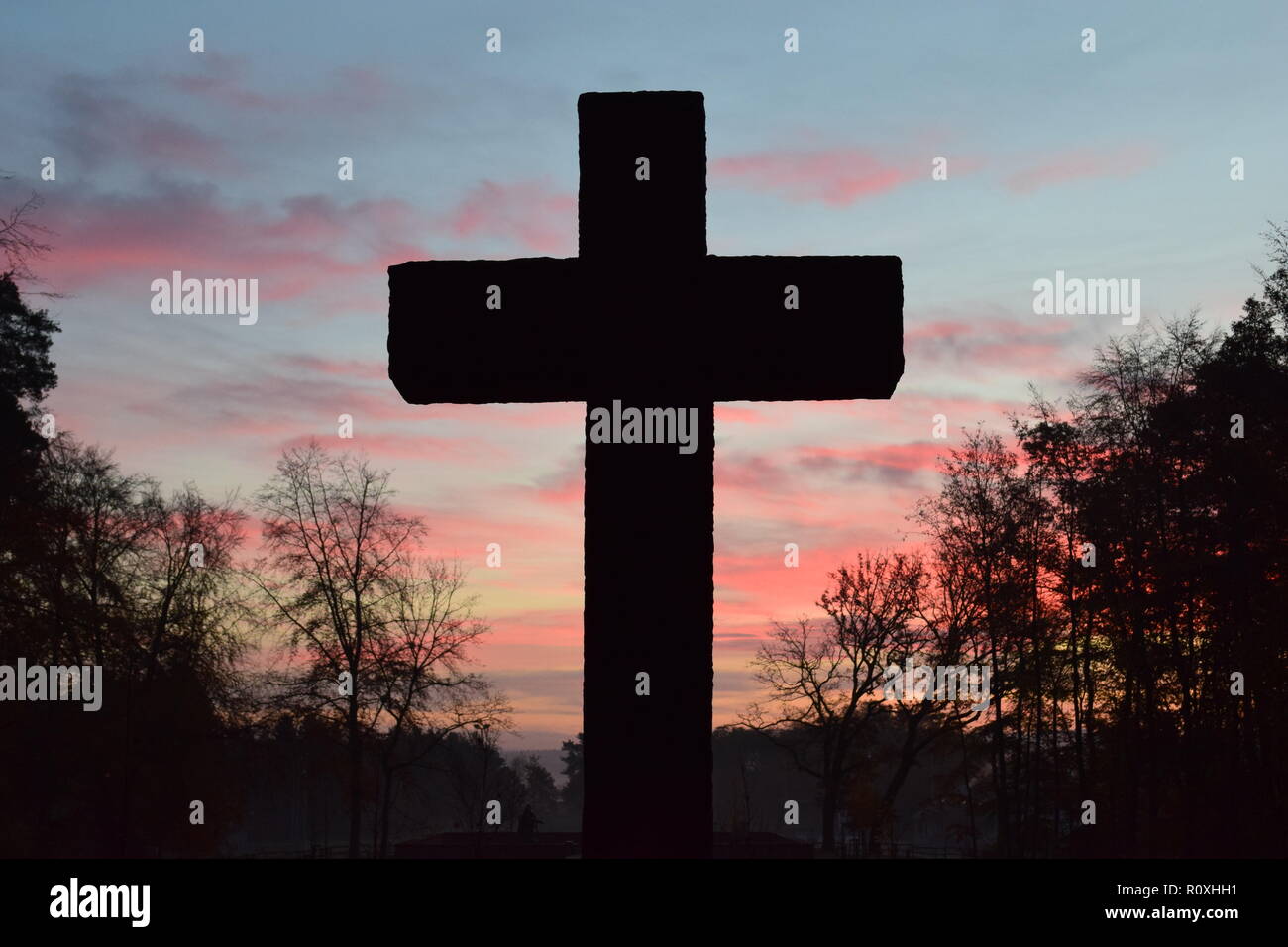 L'échéancier de l'matin ciel crépuscule vu de derrière une croix en pierre de sable au cours de sculpture le soleil levant dans le cimetière militaire Reimsbach an der Saar. Banque D'Images