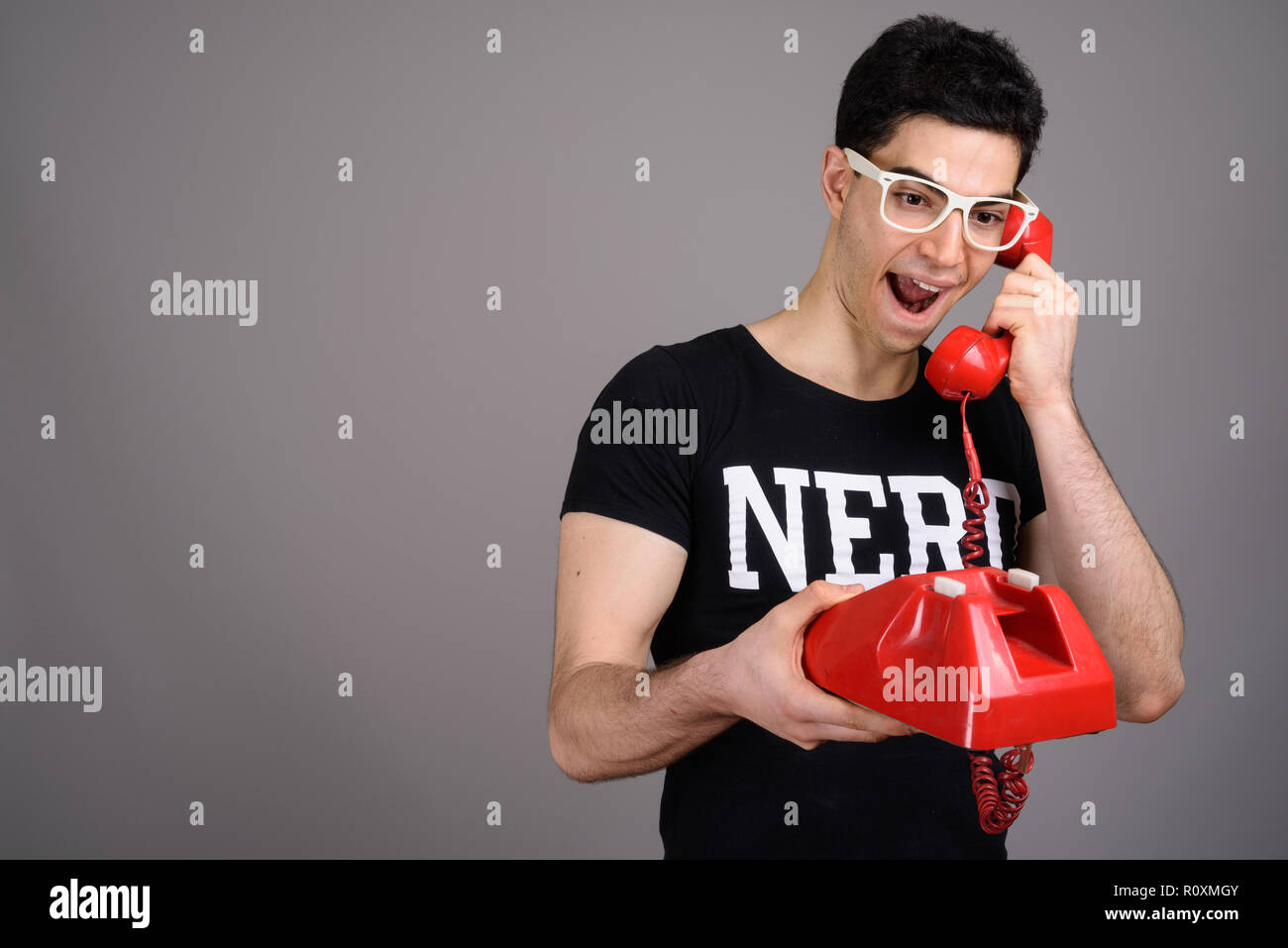 Beau jeune homme avec des lunettes nerd contre l'arrière-plan gris Banque D'Images
