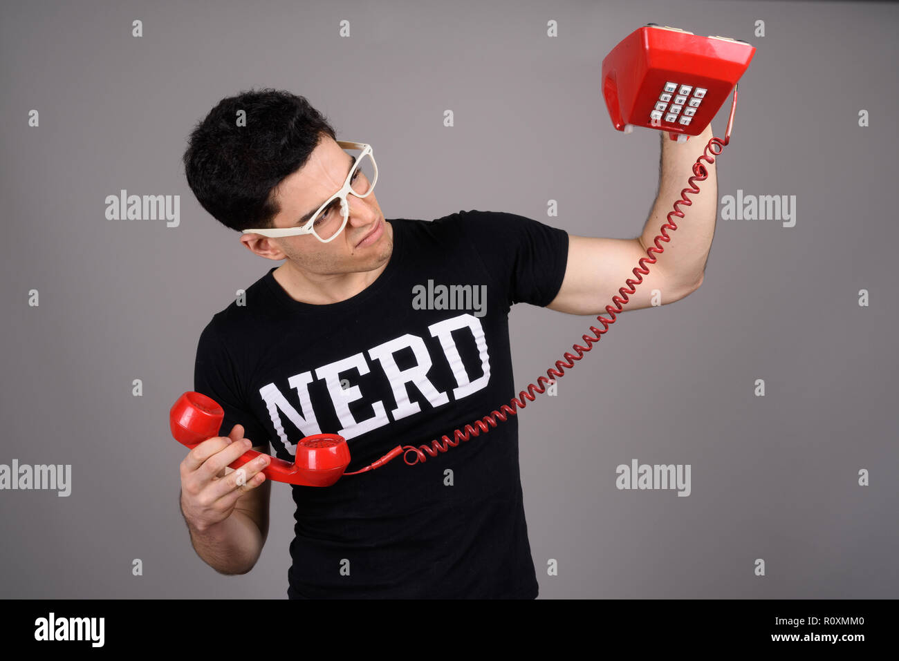 Beau jeune homme avec des lunettes nerd contre l'arrière-plan gris Banque D'Images