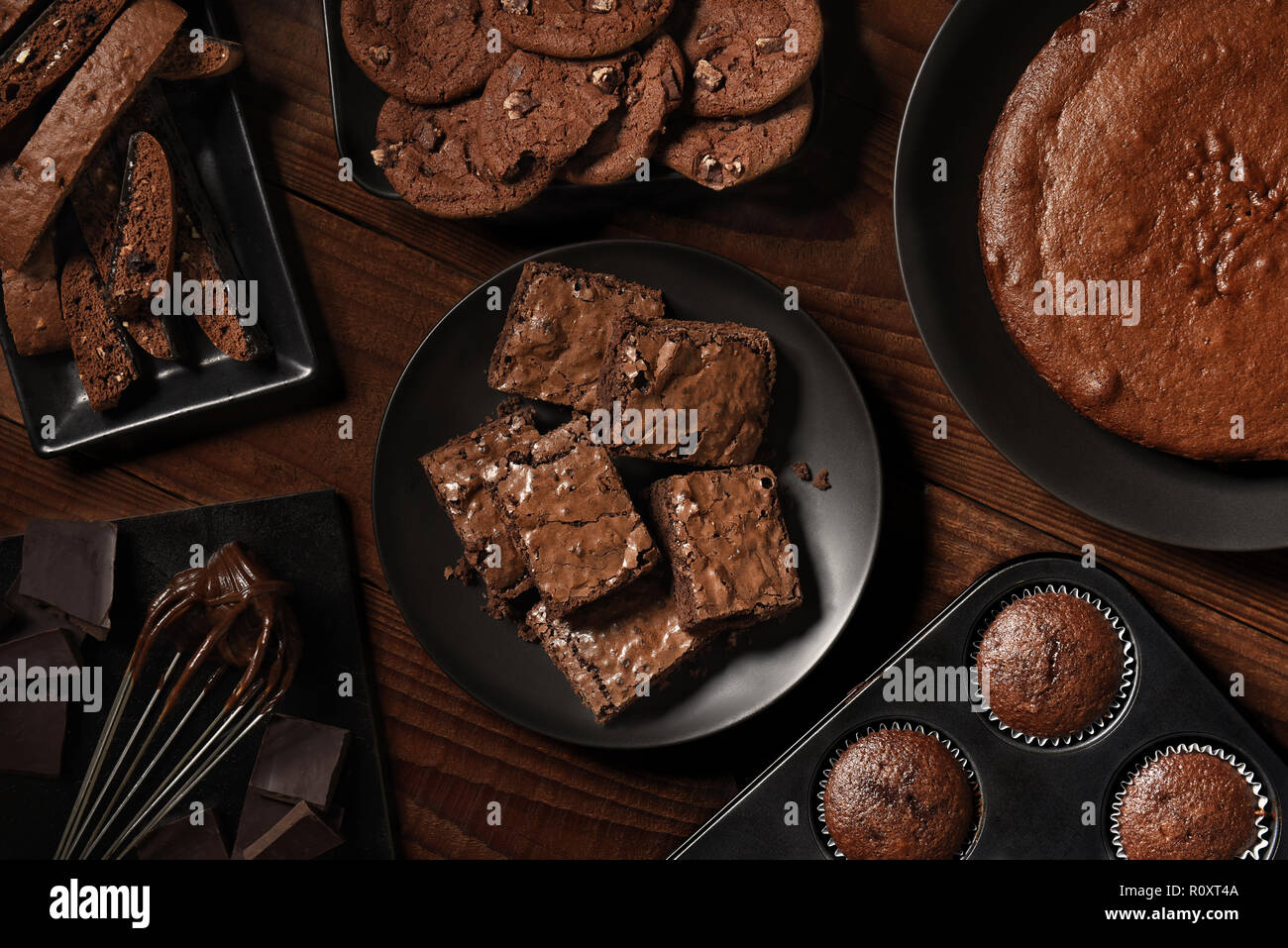 Mise à plat de l'affichage des petits desserts au chocolat sur les plaques noires et une table en bois rustique. Les articles sont, les biscuits, gâteaux, muffins, Brownies, Cookies et Banque D'Images