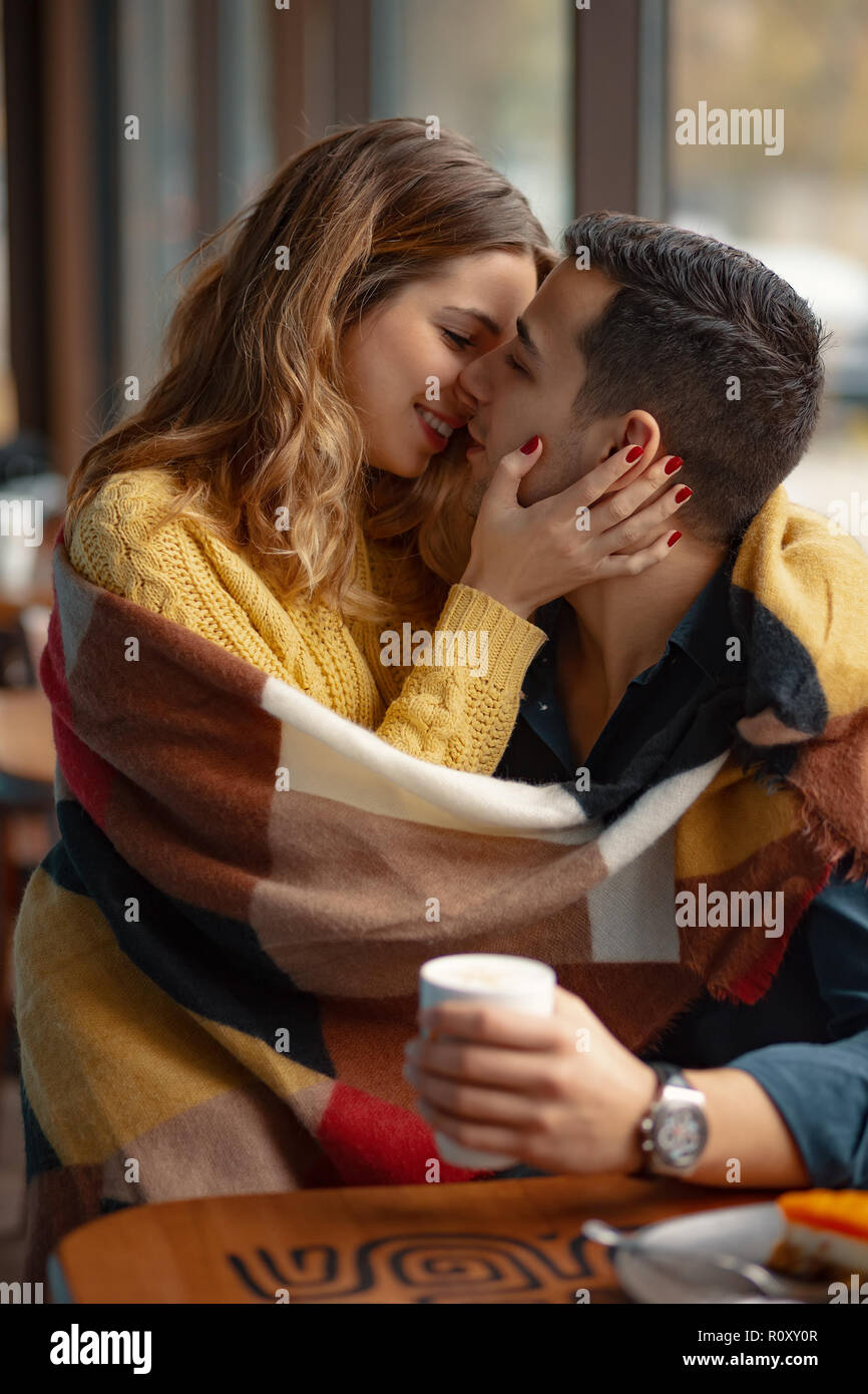 Young couple kissing et recouvert d'un plaid chaud couverture et une tasse  de café avec des fenêtres à l'arrière-plan Photo Stock - Alamy