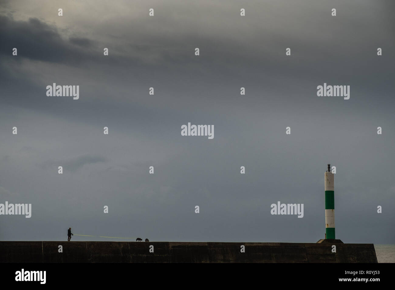 Aberystwyth, Pays de Galles, Royaume-Uni. 8 novembre, 2018. UK : Météo ciel orageux de couvaison sombre recueillir au-dessus d'un homme promenait son chien le long des murs du port à Aberystwyth car le temps tourne à nouveau pluvieux et venteux. Le Met Office ont émis un avertissement jaune pour des vents violents, de fortes pluies et la probabilité d'inondations fluviales et côtières pour de grandes parties du sud du Pays de Galles et l'ouest du pays demain matin Crédit : Keith morris/Alamy Live News Banque D'Images