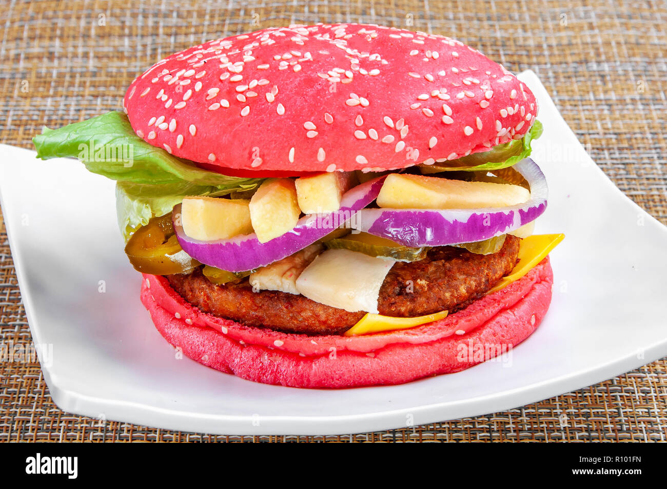 Hamburger classique avec pain rouge et légumes frais sur une assiette blanche sur fond blanc. Banque D'Images
