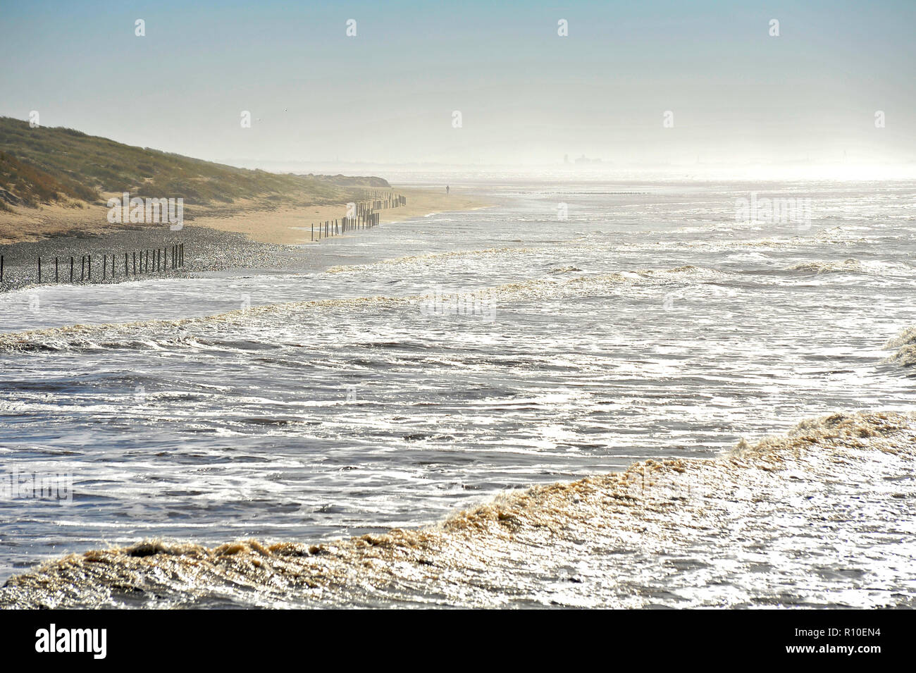 Marcher le long de la figure d'emprunt lointain plage, entre mer et dunes de sable sur jour brumeux lumineux Banque D'Images