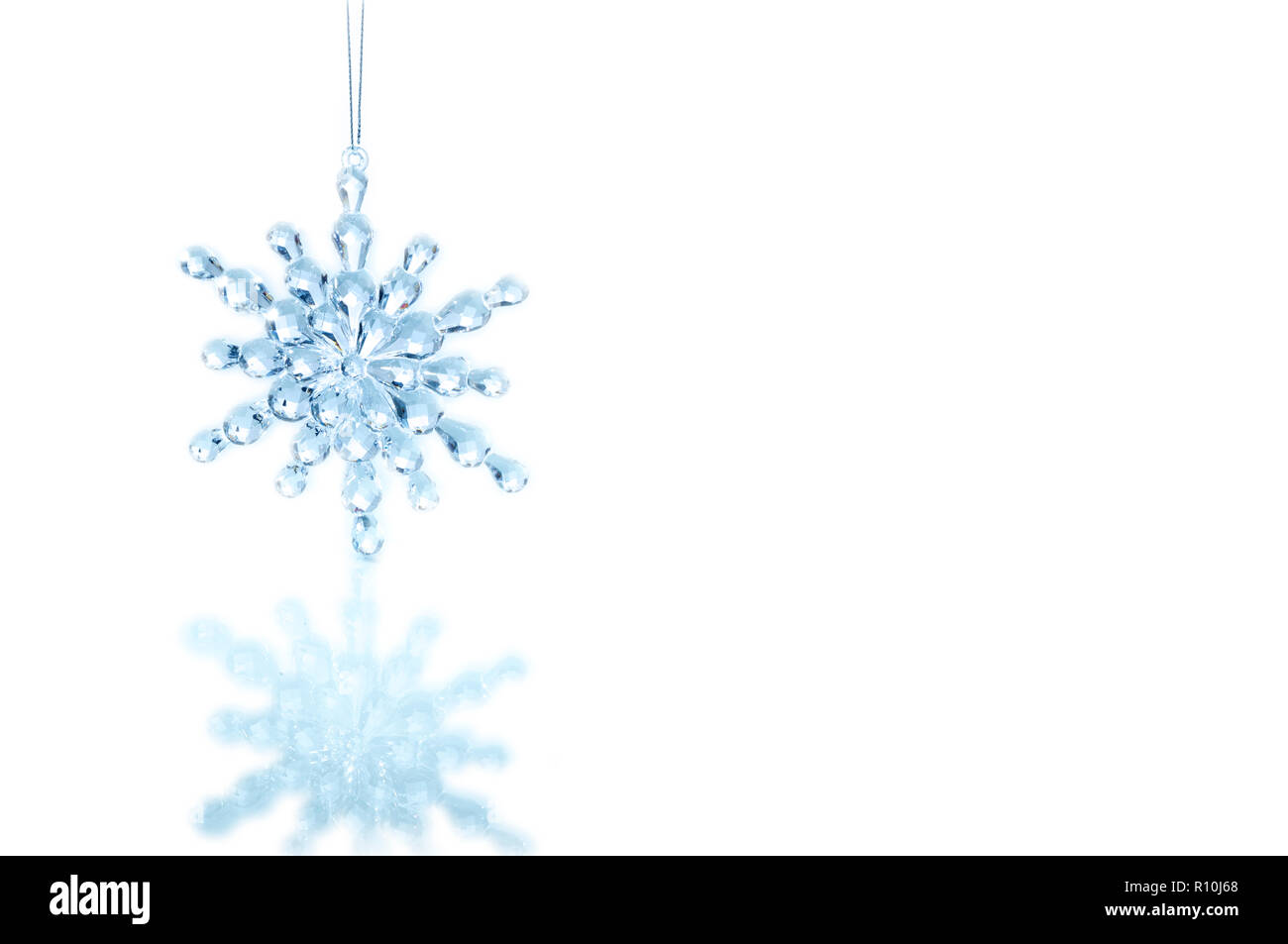 Flocon de décoration de Noël en verre suspendue au-dessus de la surface blanche avec la réflexion Banque D'Images